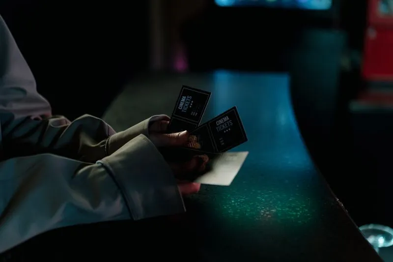 Close-up of a hand holding two cinema tickets in the dim evening light of a counter