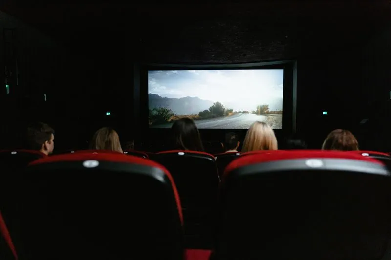 Cinema auditorium with red seats, audience seen from behind facing the bright screen