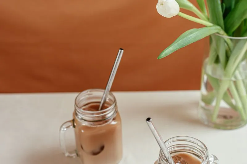 Two glasses of iced coffee with metal straws on a table, next to a vase of tulips