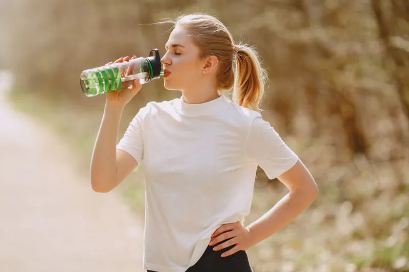 A young woman in activewear drinking from her water bottle outdoors in warm late-afternoon light