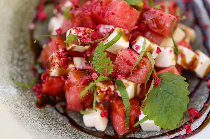 A plate of watermelon and feta cubes, scattered with fresh mint and drizzled with balsamic glaze