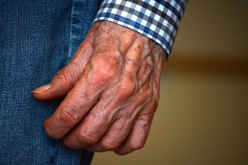 Wrinkled hand of an older person, veins visible, resting against their clothing