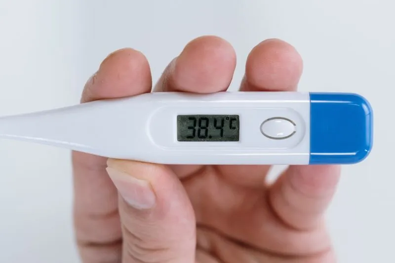 Digital medical thermometer held in hand, showing a reading of 38.4°C