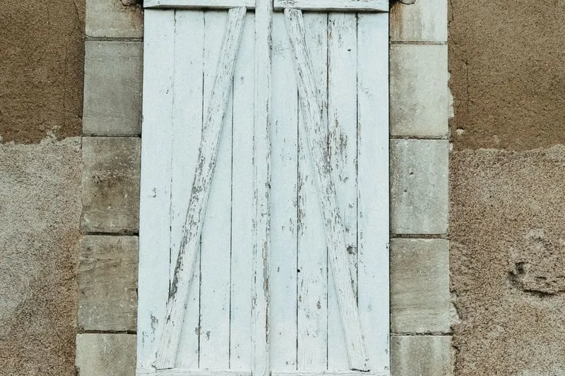 Closed white-painted wooden shutter on the stone front of an old house