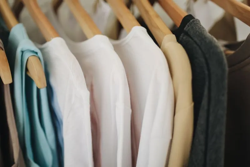 Light-coloured tops and shirts hanging on wooden hangers in a wardrobe