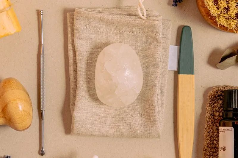 Oval, translucent alum stone resting on a beige linen cloth, surrounded by natural care accessories