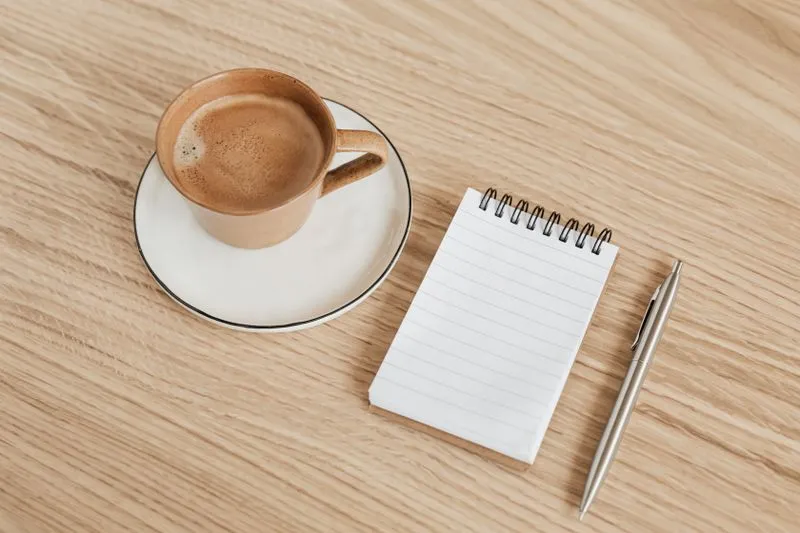 Open notebook and pen on a wooden table next to a cup of coffee