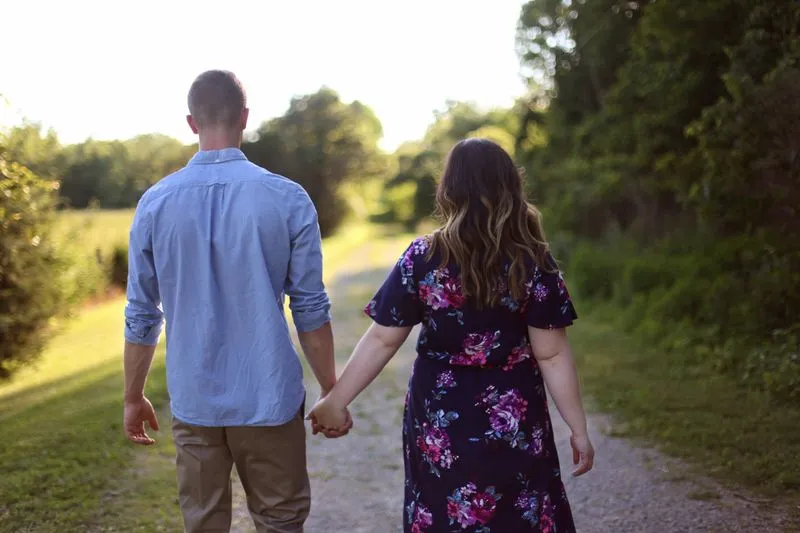 Couple holding hands, walking side by side along a tree-lined path, seen from behind