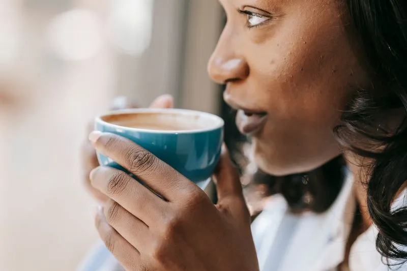 Close-up of a young woman sipping from a mug, looking towards the light of a window