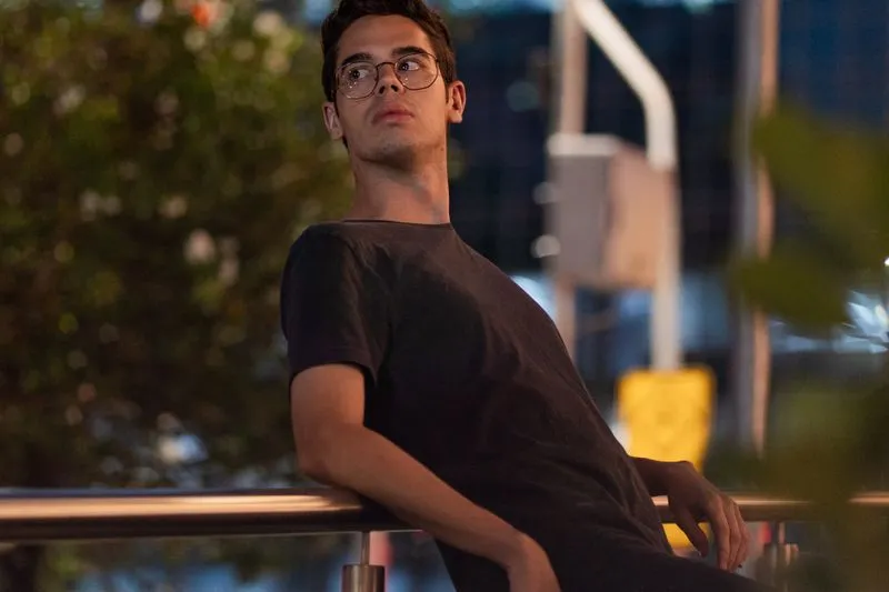 Young man in glasses leaning on a railing in the city at dusk, lost in thought