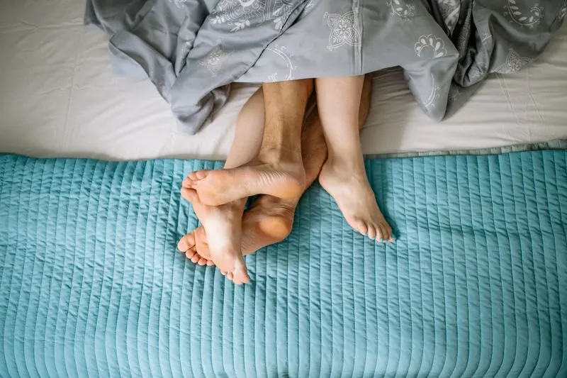 Overhead view of a couple's legs entwined under a duvet, on a bed