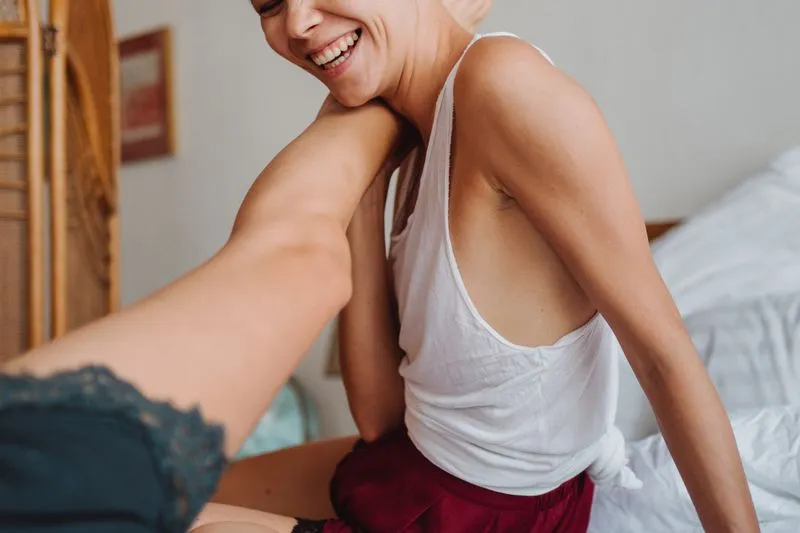 Couple laughing on a bed, one leg raised to the shoulder in a shared fit of giggles