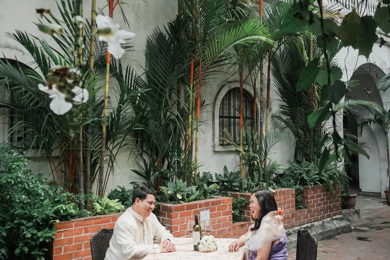 Couple at a table on a palm-shaded terrace, bordered by low brick walls