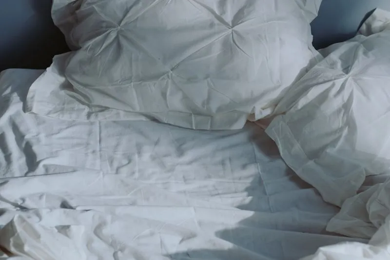 Tufted pillows and rumpled sheets on a bed, in soft light