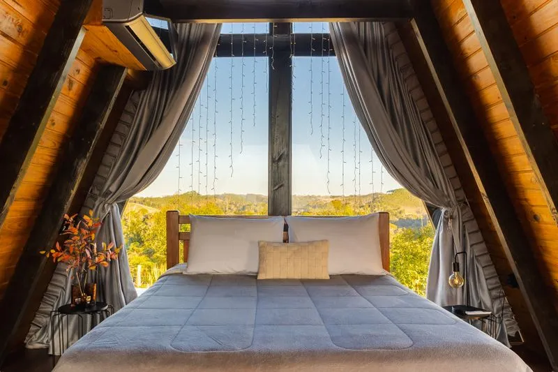 Holiday rental bedroom with a large window dressed in curtains, countryside view at dusk