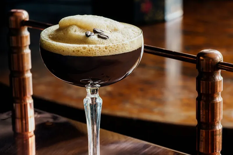 Espresso martini on the wooden counter of a cocktail bar, behind a brass rail